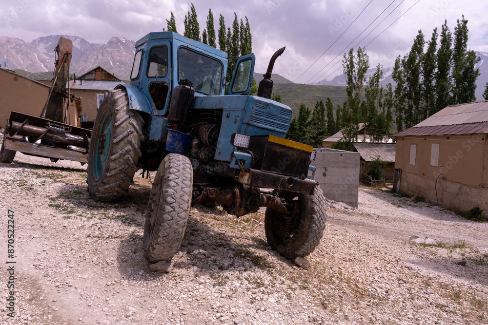 Obraz premium A blue tractor with black tires is parked in a dirt field