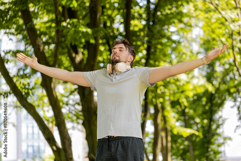 Fototapeta premium Keep calm down, relax. Bearded man jogger meditating, breathes deeply with mudra gesture, praying eyes closed, concentrated thoughts, peaceful mind outdoors. Guy exercising surrounding trees in park.