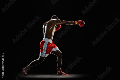 Jab punch. muscular shirtless man, boxer in red uniform practicing before match, training with intensity isolated on black background. Concept of professional sport, active lifestyle, body, strength