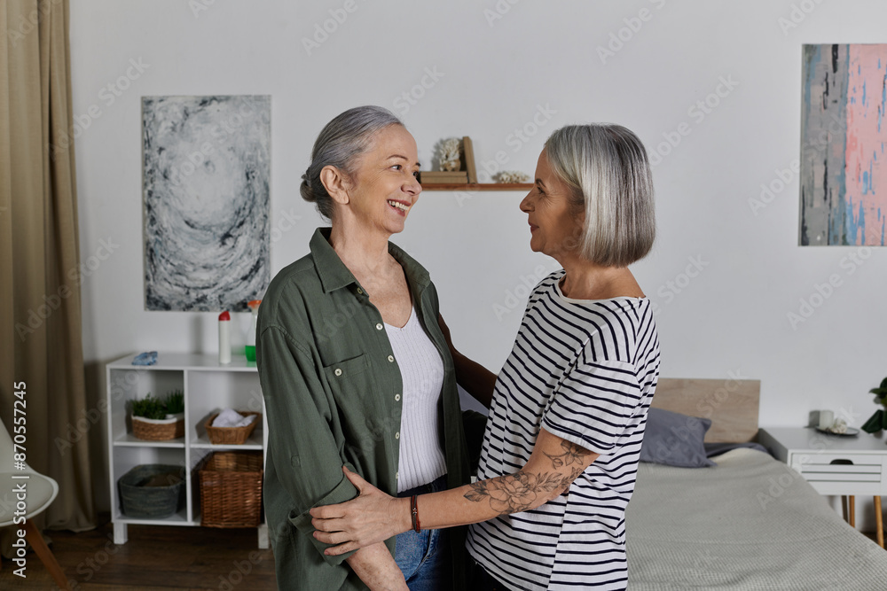 Fototapeta premium Two mature women, a lesbian couple, embrace each other in a modern apartment, their smiles radiating happiness and love.