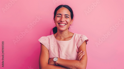 A joyful millennial woman, confidently posing with a watch and folded arms, smiling against a solid pink background