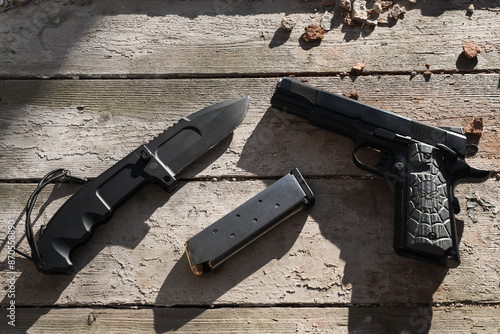 Firearms and bladed weapons, an M1911 pistol, a magazine with ammunition and a folding tactical knife on an old wooden window sill in an abandoned building. photo