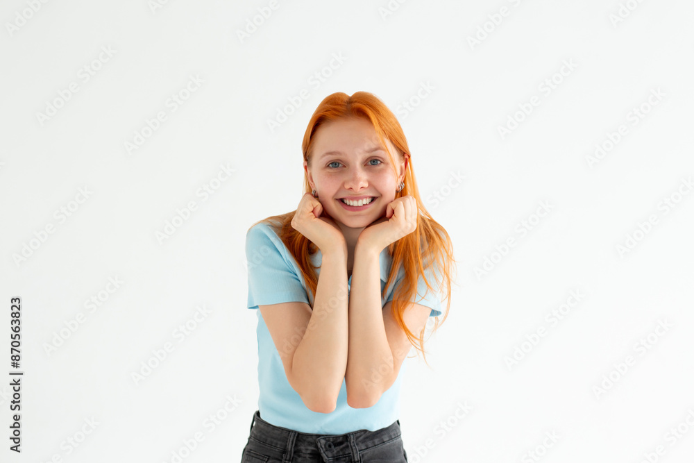 Headshot of pleased high spirit pretty female model, has warm pleasant smile, keeps hands under chin, wears blue t-shirt, isolated over white background. Happiness concept Headshot of pleased high spirit pretty female model, has warm pleasant smile, keeps hands under chin, wears blue t-shirt, isolated over white background. Happiness concept