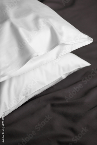 White satin (lyocell, silk, polyester) pillowcases on the bed covered with dark grey sheet. Home textile.