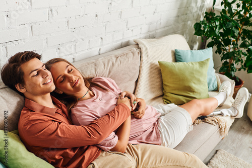 A couple relaxes on a couch, with the woman resting her head on her boyfriends shoulder.