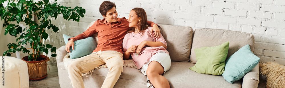 A couple sits on a couch, cuddling and smiling at each other. A couple sits on a couch, cuddling and smiling at each other.