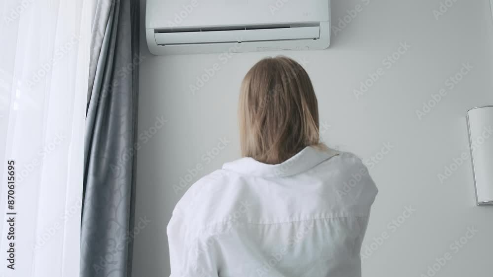 Back view of exhausted sweaty woman turning on an air conditioner with a remote control to cooling off during hot summer weather, suffering from heat, high temperature Back view of exhausted sweaty woman turning on an air conditioner with a remote control to cooling off during hot summer weather, suffering from heat, high temperature