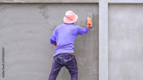 Construction worker is plastering cement on concrete fence wall structure, Backside view with copy space © Prapat