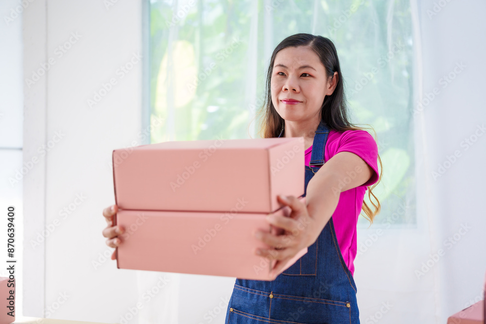 A woman in overalls sells products online, inspects parcels, takes customer orders, works at a desk, and uses pink boxes to pack items ready for shipping to customers. A woman in overalls sells products online, inspects parcels, takes customer orders, works at a desk, and uses pink boxes to pack items ready for shipping to customers.