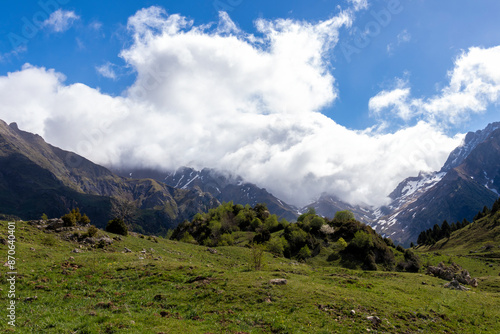 A mountain range with a cloudy sky and a green field. The sky is blue and the clouds are white