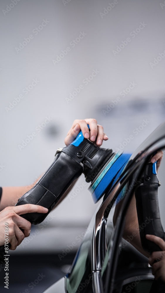 Car wash or car detailing studio employee polishes the paint of a black car using an electric polisher