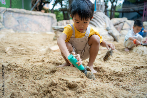 Asian kindergarten boy and girl enjoy playing in sandbox having fun on playground in sandpit.