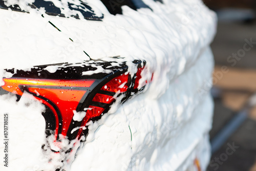 Washing Soap and Foam. Close Up Shot of Foam Dripping from Car's Rear Wheel Arch onto the Electric Car's Tyre and Rim.Summer Car Washing. Cleaning Car Using High Pressure Water and shampoo.
