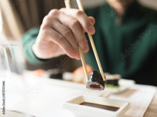 Close-up of sushi roll held by chopsticks above soy sauce. Roll is fresh and perfectly formed. Hand holding chopsticks is out of focus, focusing on culinary aesthetic