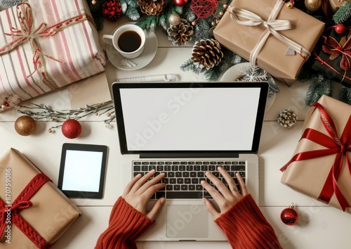 A person is typing on a laptop with a cup of coffee beside them, surrounded by Christmas gifts, capturing a festive work-from-home atmosphere. © Mike