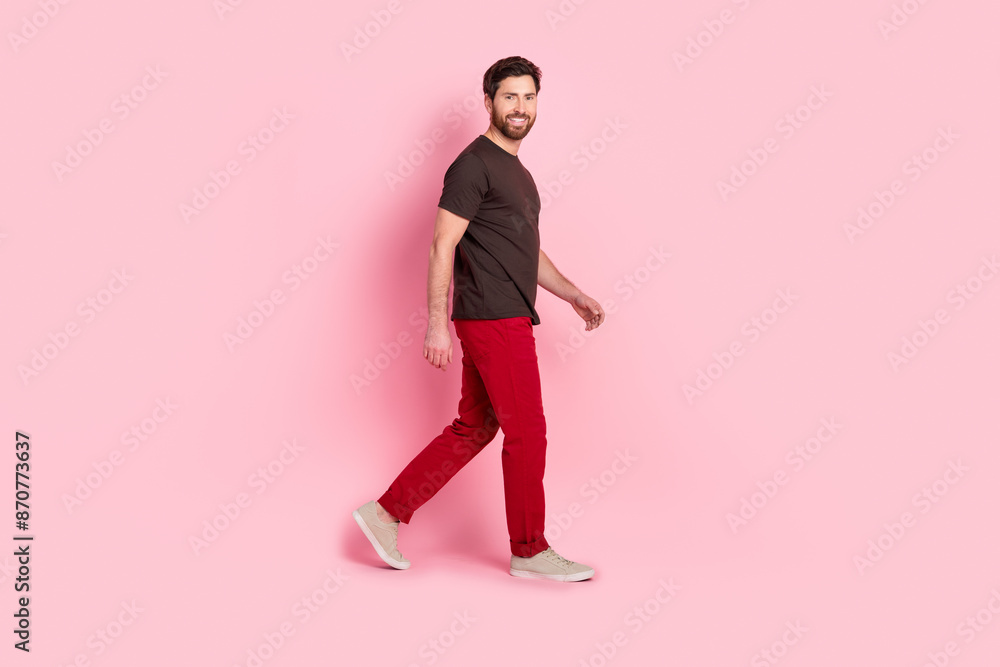 Full length photo of optimistic man with bristle dressed brown t-shirt red pants walk empty space isolated on pink color background Full length photo of optimistic man with bristle dressed brown t-shirt red pants walk empty space isolated on pink color background