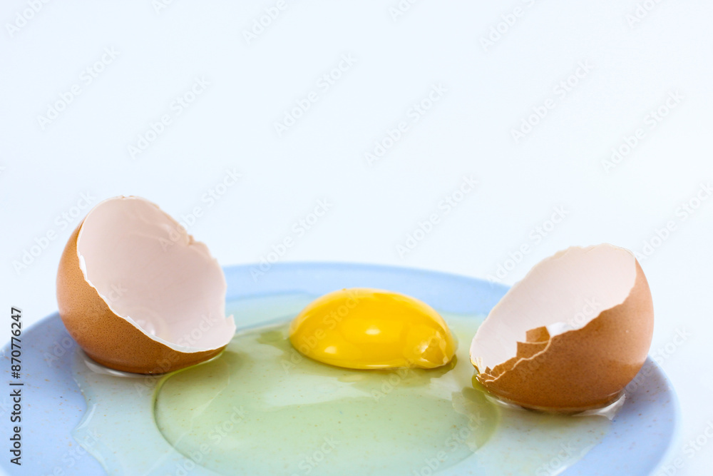Cracked raw eggs on a small bluish plate with a white isolated background Cracked raw eggs on a small bluish plate with a white isolated background