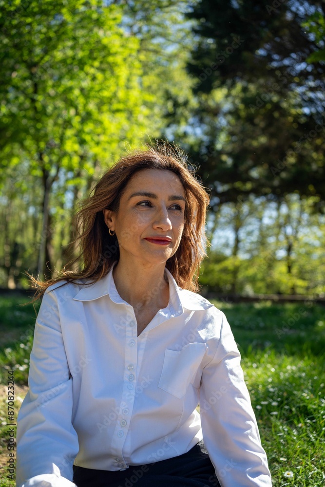 Middle-aged woman in a white shirt sitting in a sunny park Middle-aged woman in a white shirt sitting in a sunny park