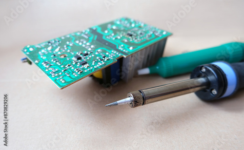 Electronic repair equipment. Soldering iron and desoldering pump in front of the circuit board. Focused on soldering iron tip. photo