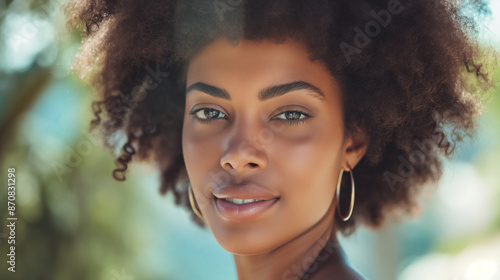A woman with curly hair and gold hoop earrings is smiling. She has a natural, relaxed look on her face