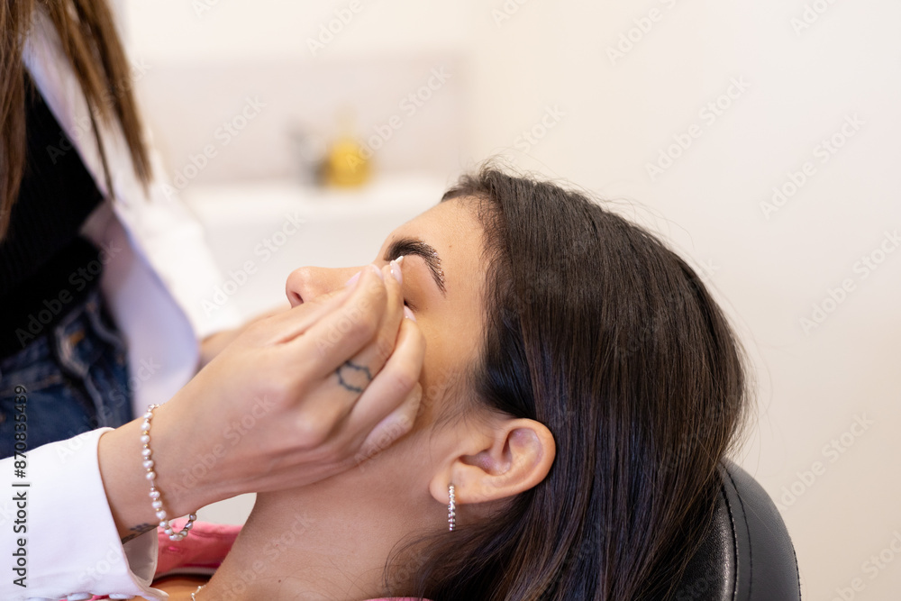 Fototapeta premium Beautician making eyebrow design and shading procedures. Young latin woman in a professional beauty salon for threading and brow shape correction