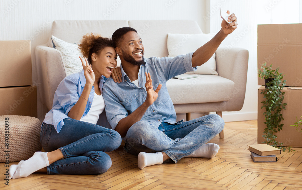 Happy House Owners. Afro Couple Taking Selfie With Smartphone Gesturing Victory Sign After Moving Into New Home. Copy Space Happy House Owners. Afro Couple Taking Selfie With Smartphone Gesturing Victory Sign After Moving Into New Home. Copy Space