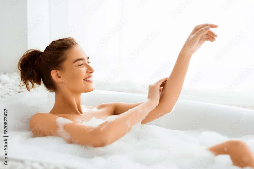 Happy woman washing body and feel relax in bathtub with foam