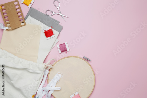 Embroidery set fot stitching. Beige cotton cloth in embroidery hoop on pink background with fabric, colorful threads, scissors and needls photo