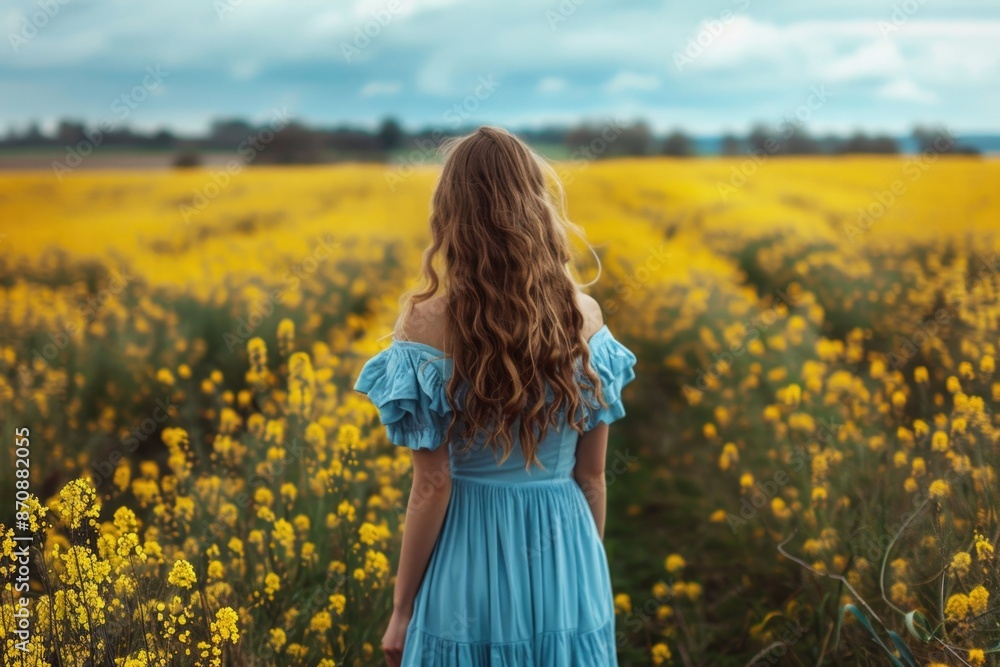 A woman stands amidst a vibrant field of yellow flowers, with the sun shining down on her