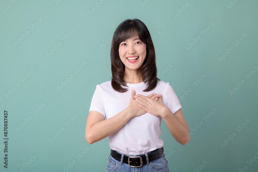 Smiling positive, pretty asian young woman holding heart with hands on light green background. Smiling positive, pretty asian young woman holding heart with hands on light green background.