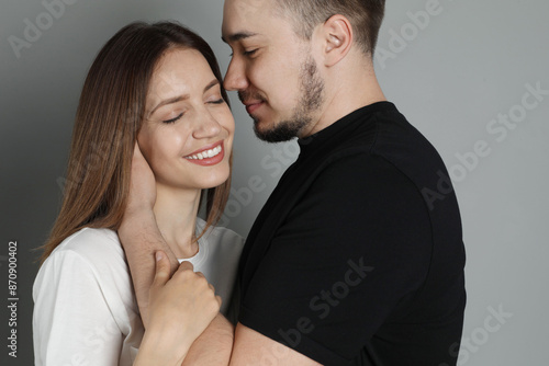 Man hugging and kissing his happy girlfriend on grey background