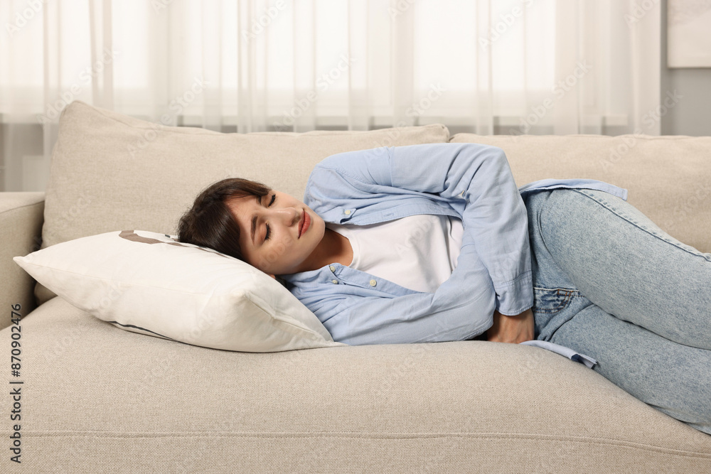 Upset woman suffering from abdominal pain on sofa at home Upset woman suffering from abdominal pain on sofa at home