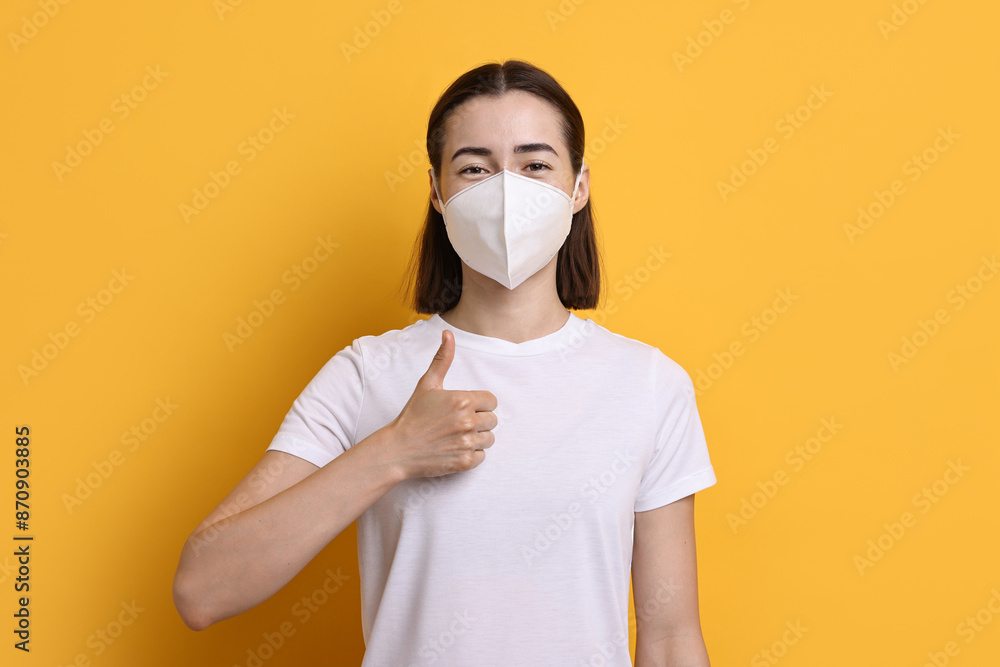 Woman in respirator mask showing thumbs up on orange background Woman in respirator mask showing thumbs up on orange background