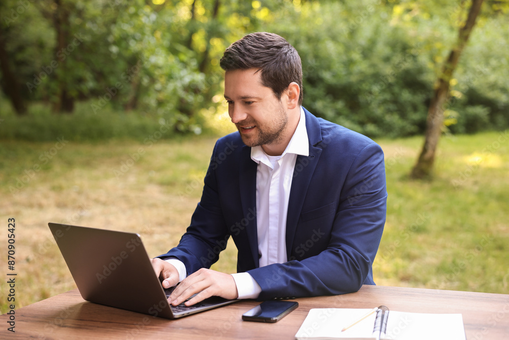 Smiling businessman working with laptop at table outdoors. Remote job Smiling businessman working with laptop at table outdoors. Remote job