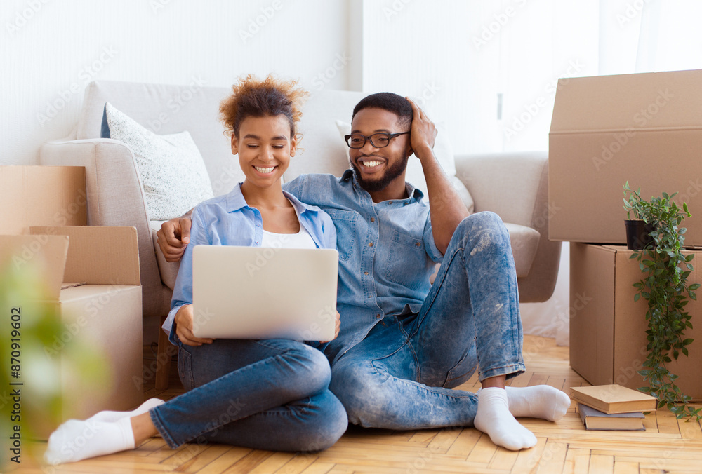 Moving House. Happy African American Couple Using Laptop Sitting On Floor Among Unpacked Cardboard Boxes In New Home. Selective Focus Moving House. Happy African American Couple Using Laptop Sitting On Floor Among Unpacked Cardboard Boxes In New Home. Selective Focus