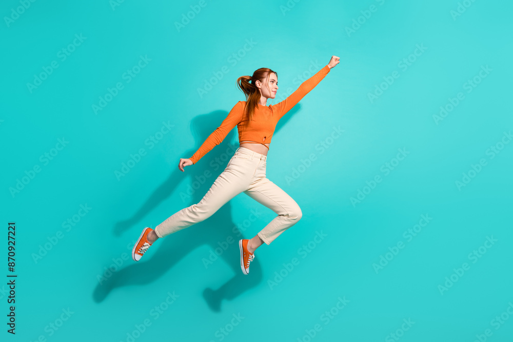 Fototapeta premium Full length photo of strong woman wear crop top white pants raising fist up fly to empty space isolated on turquoise color background