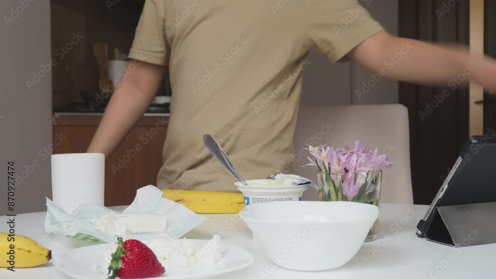 teenage boy at home in the kitchen eating a delicious healthy breakfast. Healthy breakfast, cottage cheese with fruit (strawberry and banana), fresh orange juice. Organic natural diet concept. teenage boy at home in the kitchen eating a delicious healthy breakfast. Healthy breakfast, cottage cheese with fruit (strawberry and banana), fresh orange juice. Organic natural diet concept.