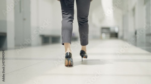 A woman wearing high heels walks down a hallway. Concept of elegance and sophistication, as the woman's attire and posture suggest that she is attending a formal event or going to work