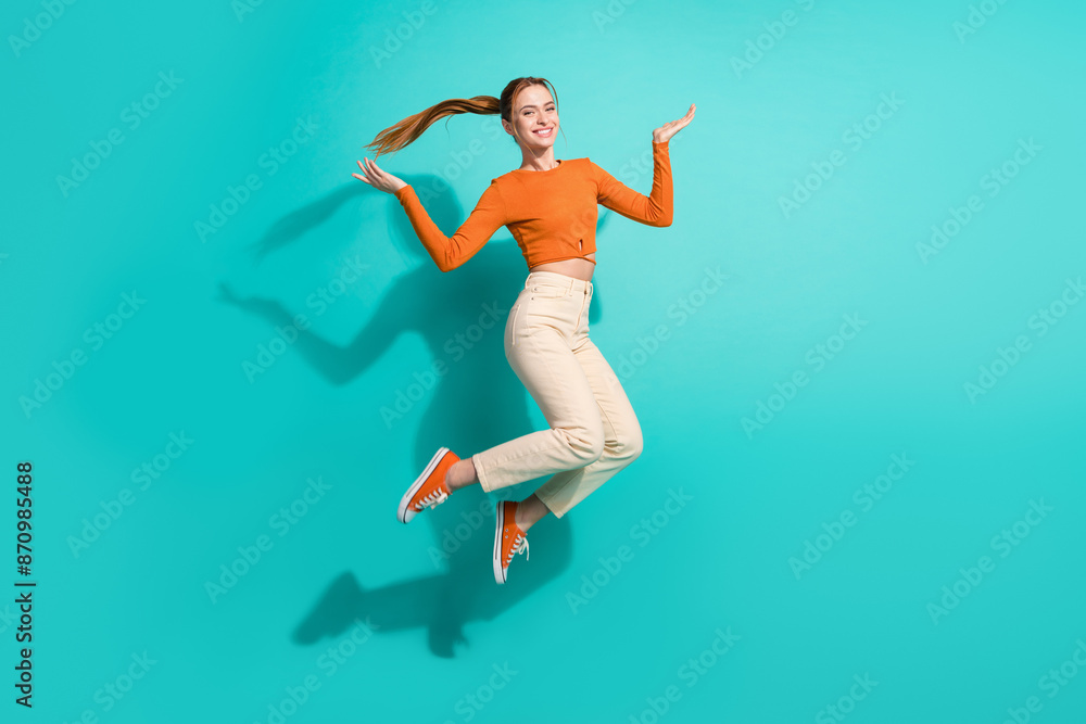 Full size photo of good mood girl dressed orange shirt pants palms presenting objects empty space isolated on teal color background Full size photo of good mood girl dressed orange shirt pants palms presenting objects empty space isolated on teal color background
