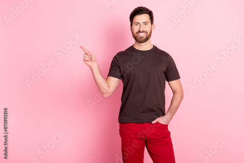 Photo of optimistic guy with stylish stubble dressed brown t-shirt indicating at promotion empty space isolated on pink color background © deagreez