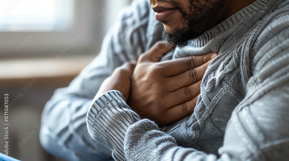 Close-up of a man holding his chest in discomfort, wearing a grey sweater. Concept of heart health, pain, or anxiety. Close-up of a man holding his chest in discomfort, wearing a grey sweater. Concept of heart health, pain, or anxiety.