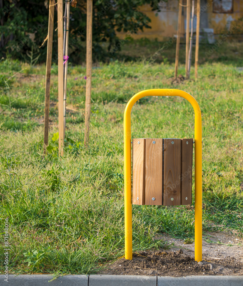 Fototapeta premium Yellow metal and wood trash can in a park with green grass