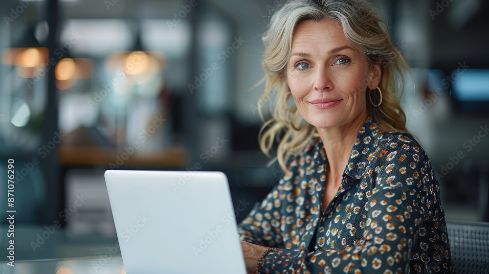 An elegant woman with light hair, sitting in an office with a laptop, subtly smiling as she looks ahead, reflecting a blend of confidence and approachability professional vibe. An elegant woman with light hair, sitting in an office with a laptop, subtly smiling as she looks ahead, reflecting a blend of confidence and approachability professional vibe.