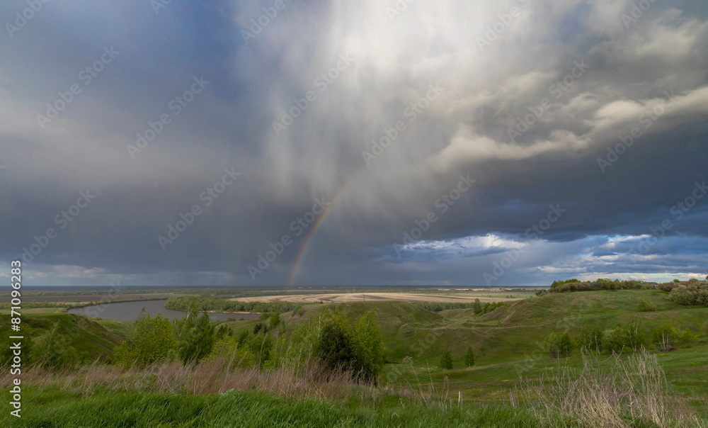 A tranquil rural landscape under a dramatic sky, where a rainbow stretches across the horizon, casting a spectrum of colors over the rolling hills and agricultural fields. A tranquil rural landscape under a dramatic sky, where a rainbow stretches across the horizon, casting a spectrum of colors over the rolling hills and agricultural fields.