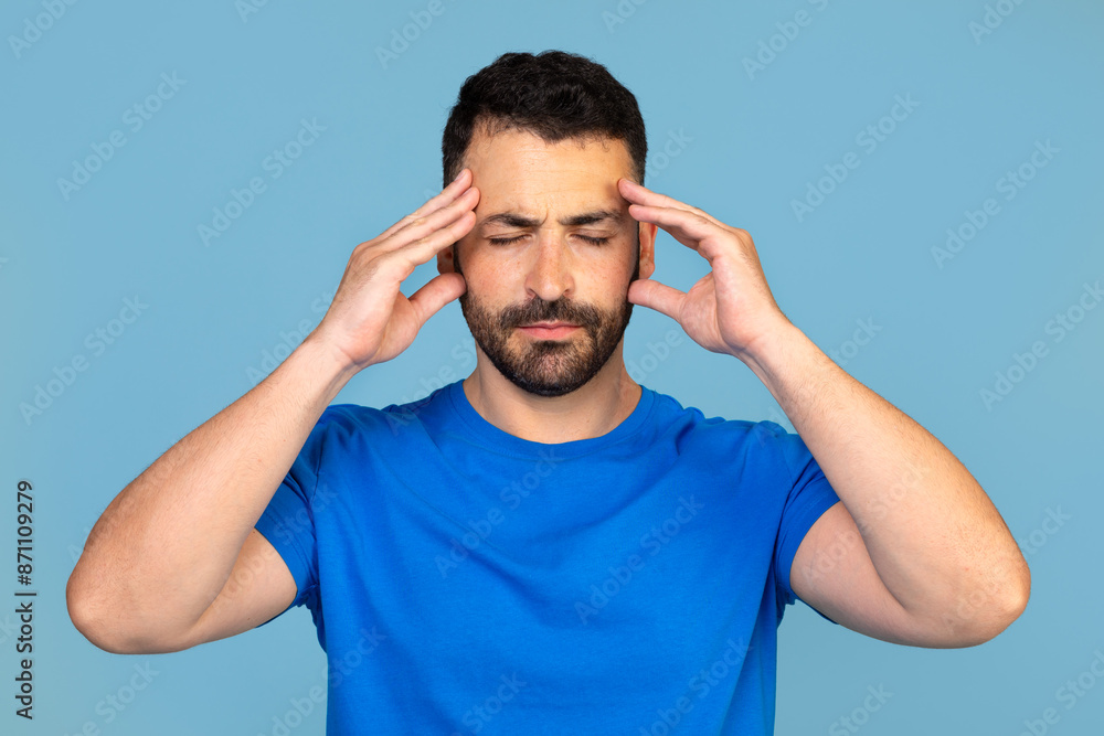 Middle-aged man with headache touching his temples, emotional photo on blue studio background, empty space. Upset man rubbing his lightened with red forehead, having migraine Middle-aged man with headache touching his temples, emotional photo on blue studio background, empty space. Upset man rubbing his lightened with red forehead, having migraine