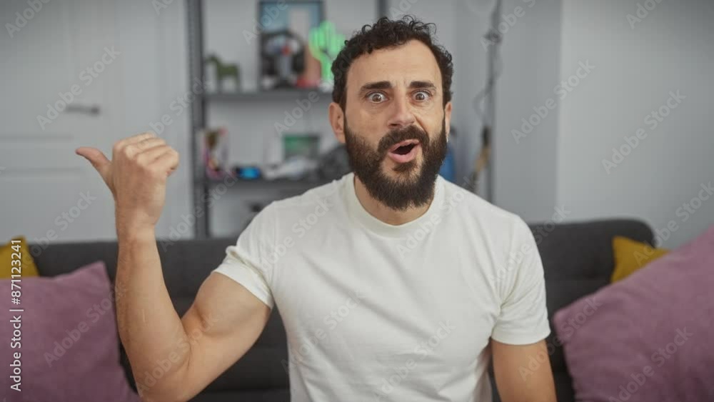 Surprised middle age man, pointing to the side with amazed expression, wearing white t-shirt, at home. open mouth indicating towards amazing discovery indoors. Surprised middle age man, pointing to the side with amazed expression, wearing white t-shirt, at home. open mouth indicating towards amazing discovery indoors.