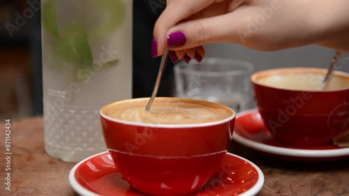 Close up of a female hand stirring espresso coffee in a red cup on a cafe table