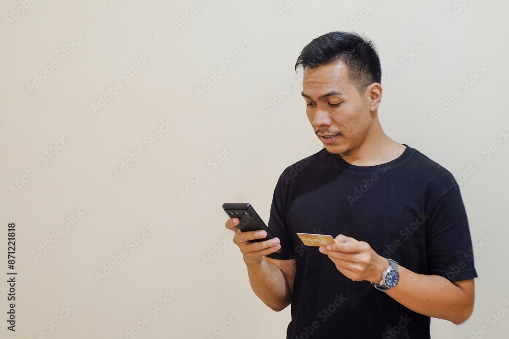 A Southeast asian man holding credit card and mobile phone to pay online shopping, on color background, technology, finance. A Southeast asian man holding credit card and mobile phone to pay online shopping, on color background, technology, finance.