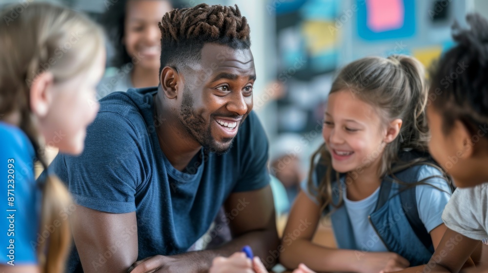 Obraz premium Teacher smiling and engaging with a group of happy children in a lively classroom, fostering a nurturing and vibrant educational environment through interactive discussion and learning.