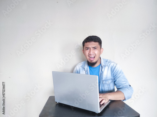 Adult Asian man sitting in front of his laptop showing shocked face expression photo